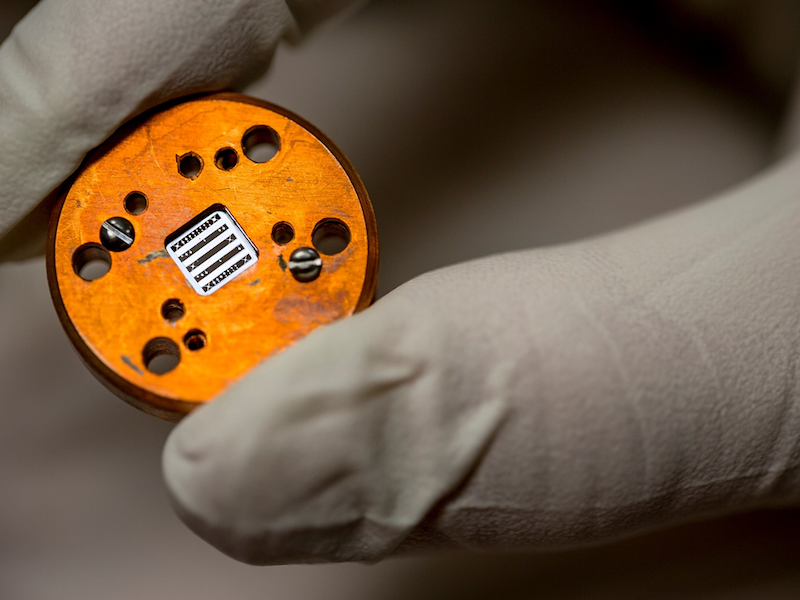 gloved hand holding a chip used to detect gravitational waves