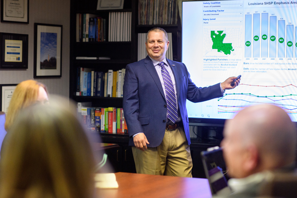 Man points to projector screen in conference room.