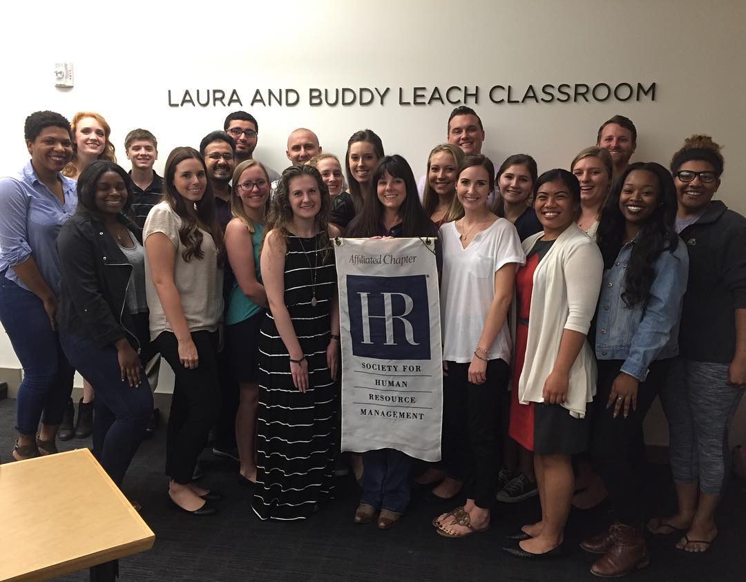 SHRM organization students stand with group flag at chapter meeting.