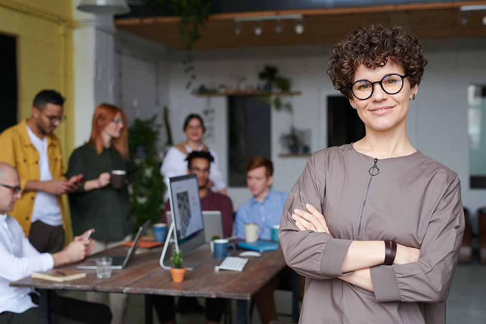 woman with glasses standing in front of group in a meeting