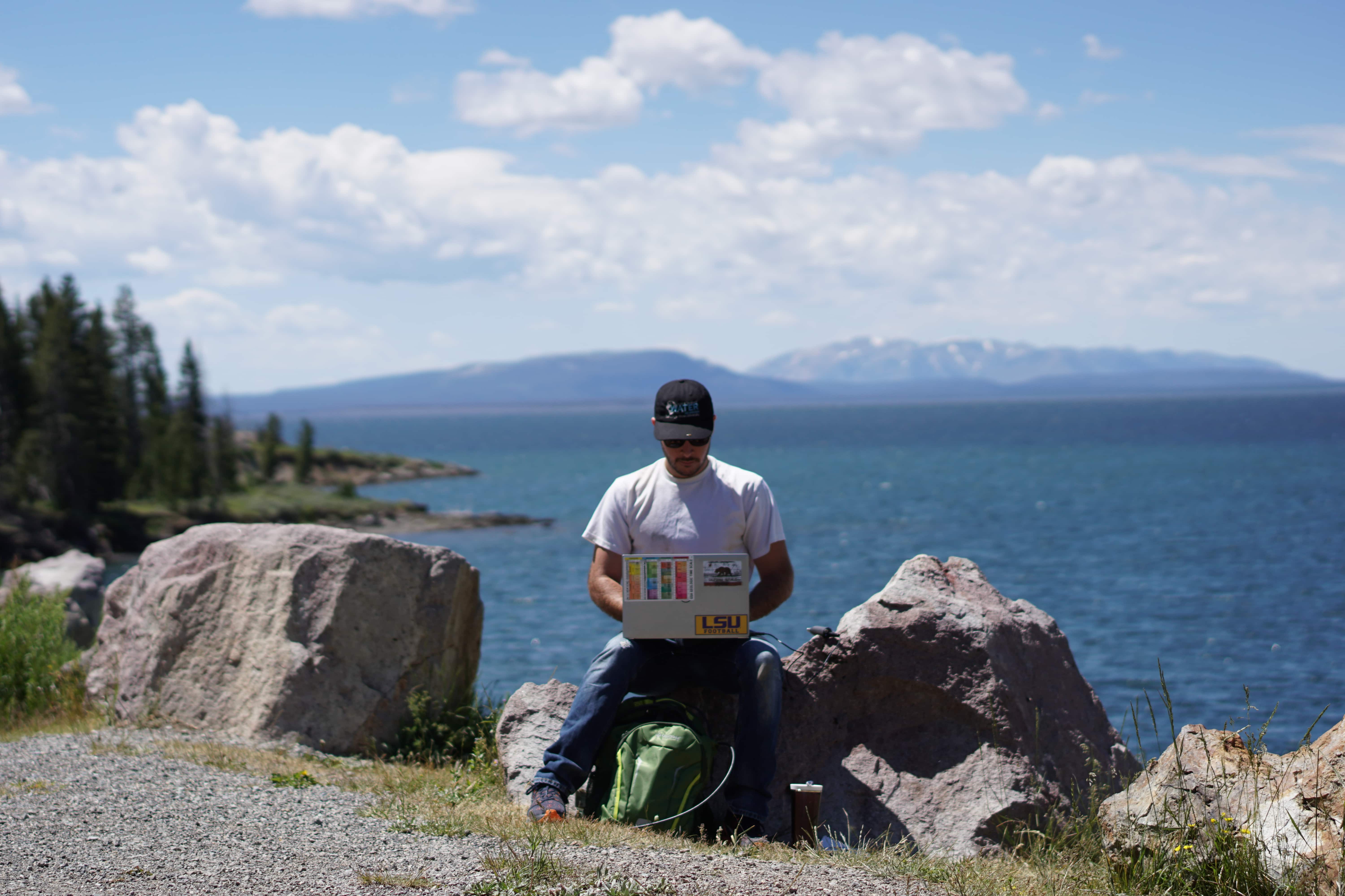 A student sittying on a rock and on their laptop